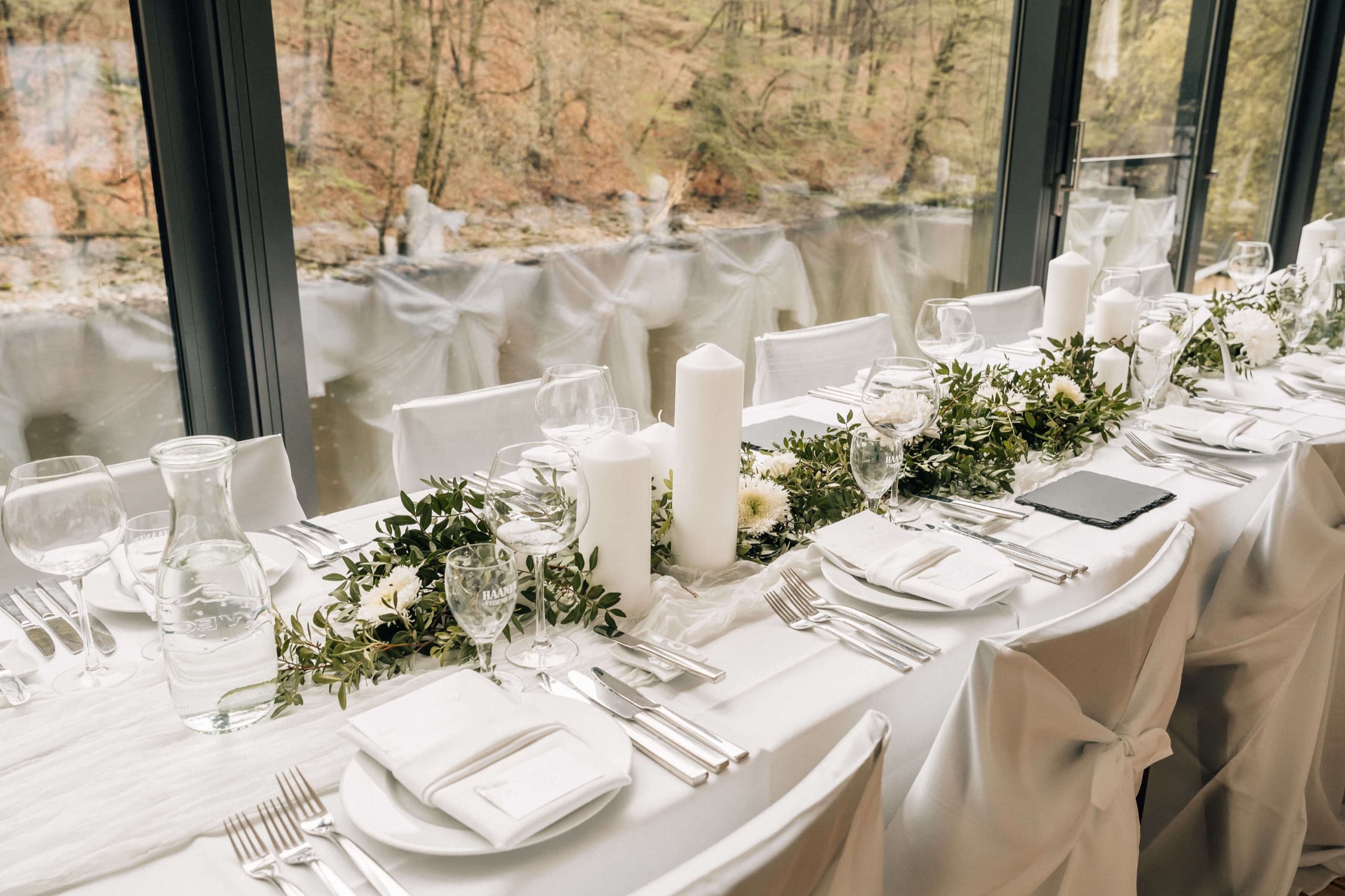 Festlich gedeckte lange Tafel an der Fensterfront mit Blick in den Wald