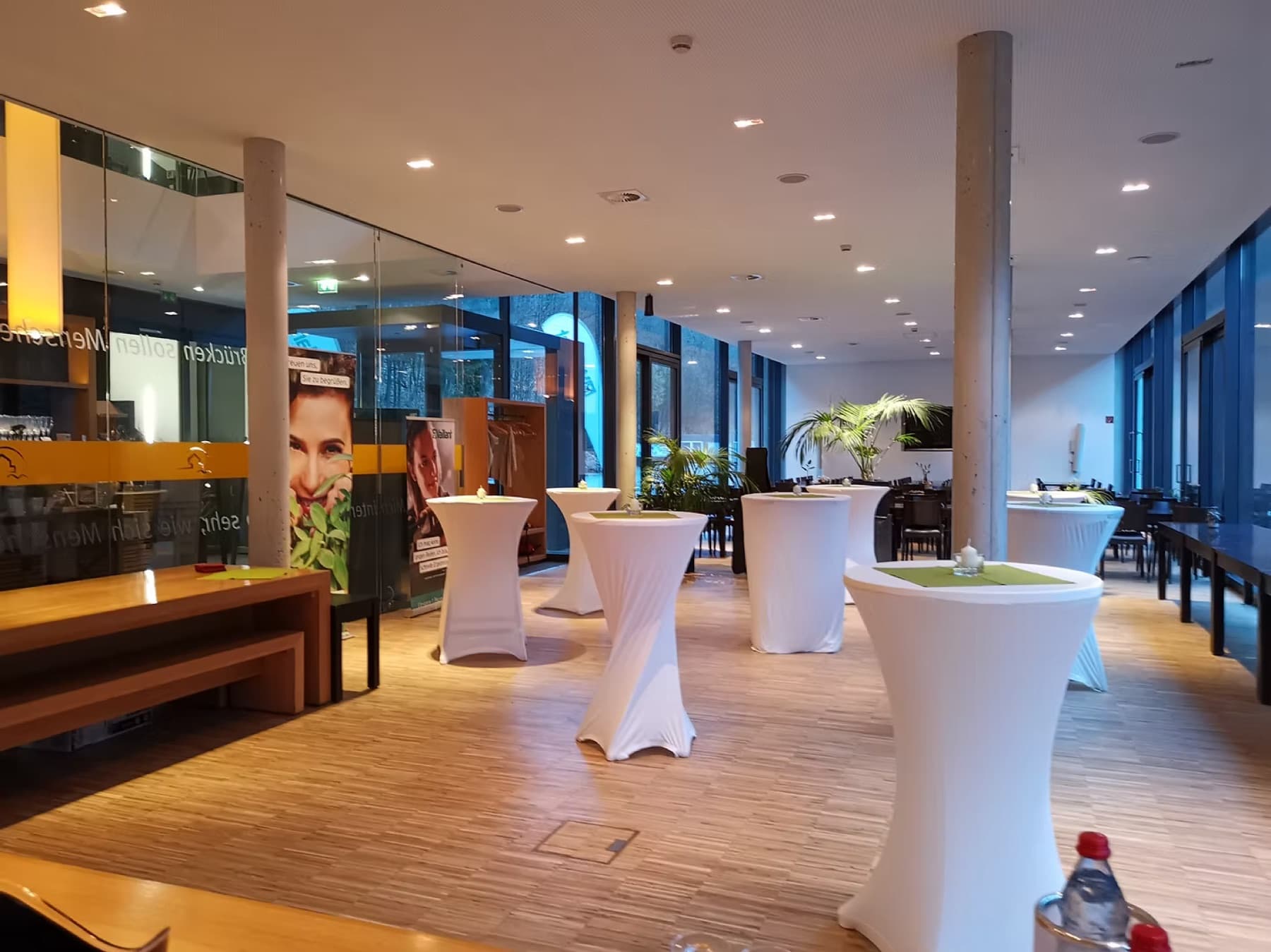 Heller Saal mit eingedeckten Stehtischen, Holzboden und Fensterfront zum Tal