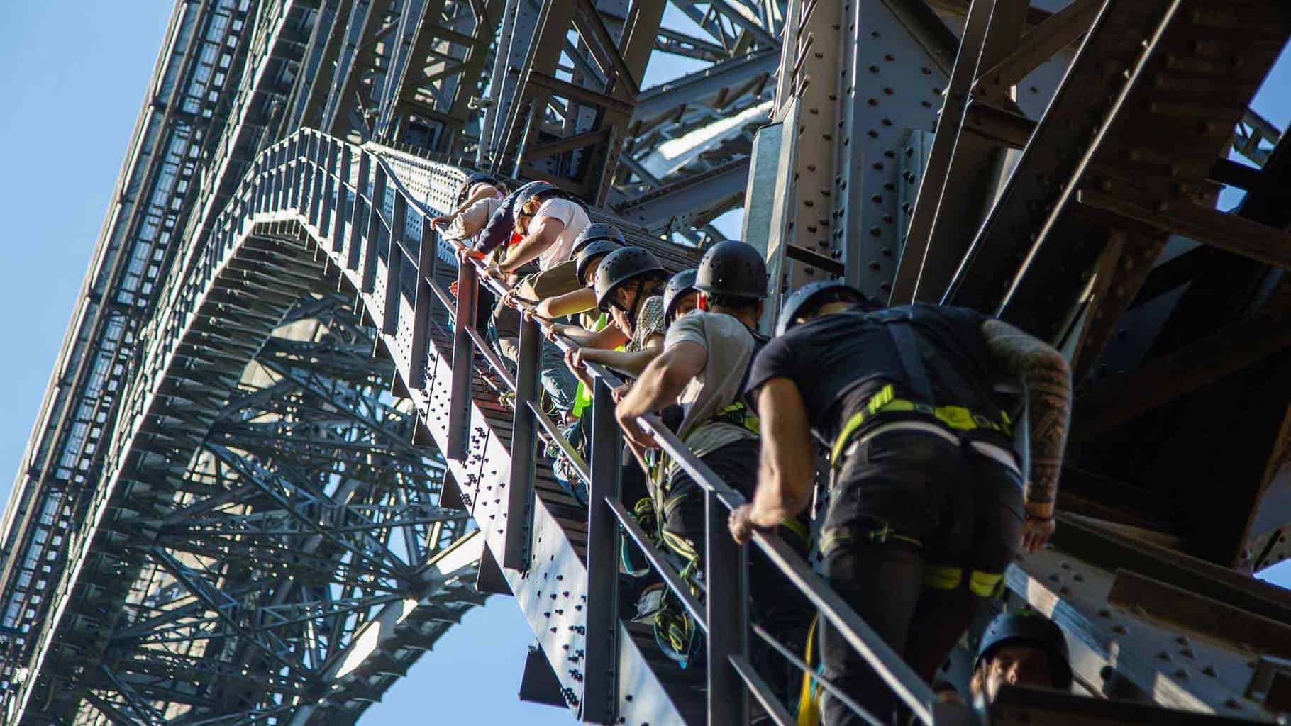 Gruppe mit Helmen und Klettergurten steigt über die Stufen am Stahlbogen der Müngstener Brücke hinauf
