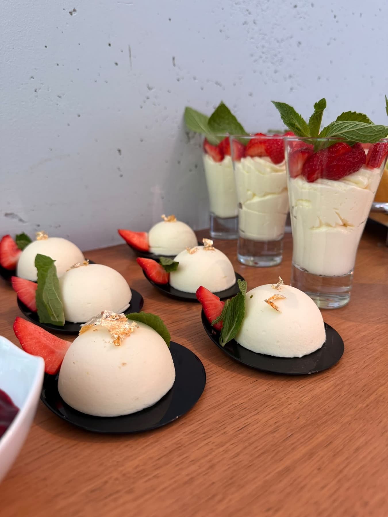 Desserts mit Blattgold und Erdbeere, dahinter Süßes im Glas mit Minze